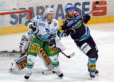 #28 Brad Tiley, Verteidiger, Liwest Black Wings Linz vor dem Tor der Laibacher, bedraengt von der #27 Jeremiah McCarthy, Olimpija Laibach.